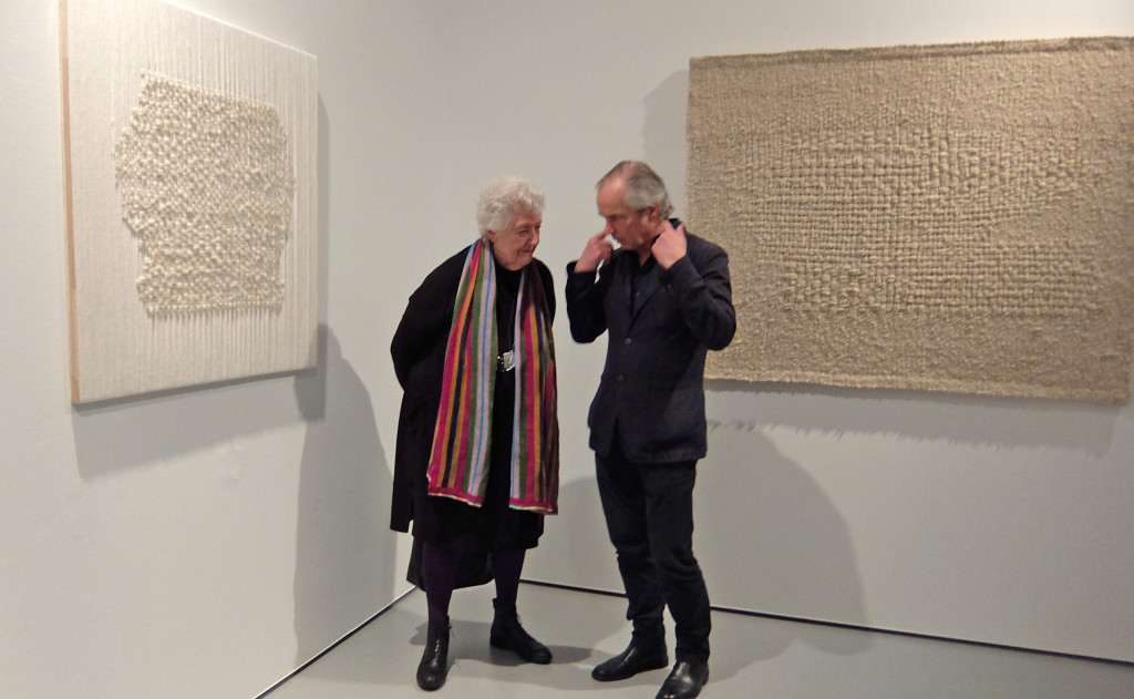 Sheila Hicks with visitor; to the left "Conversation", 2016; to the right "White letter II", 1961, collection Stedelijk Museum Amsterdam; Hicks calls her experimental monochrome tapestries "Hieroglyphs and letters"